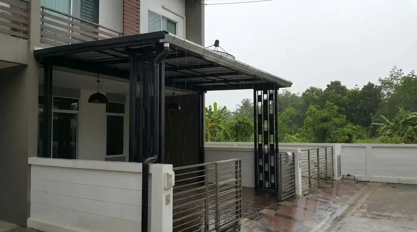 Steel-framed metal sheet roof with a gutter and downpipe in front of a two-storey townhouse, in the rain on wet paving